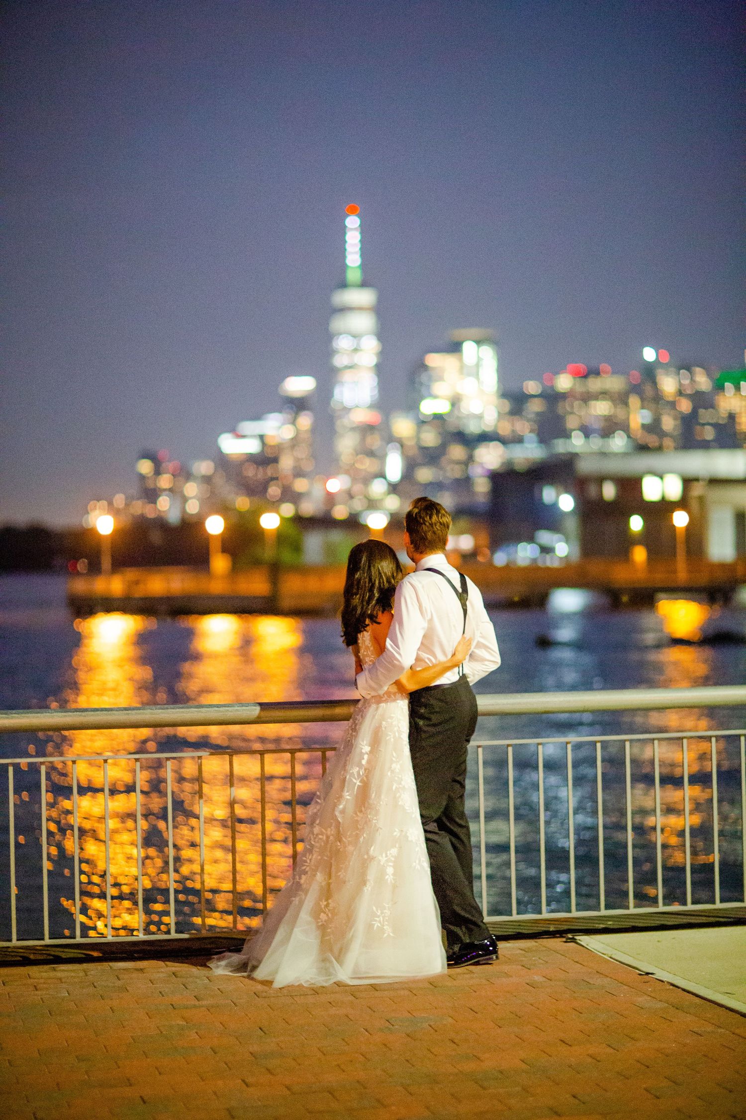 Romantic nighttime cityscape wedding photos with illuminated skyline across the water.