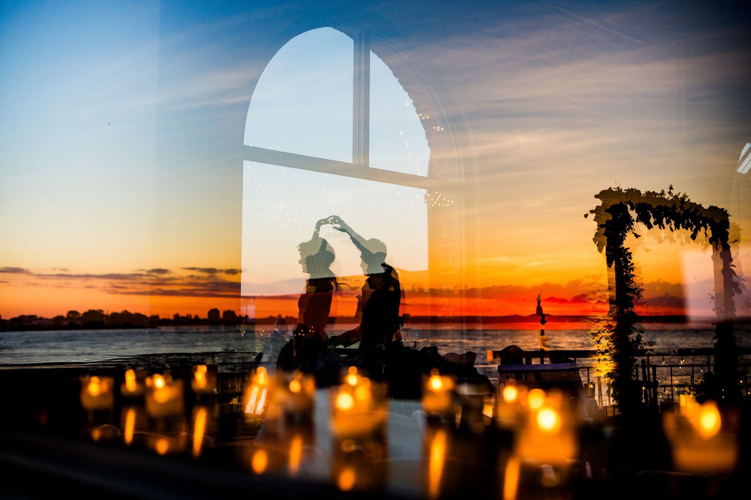 Silhouettes of wedding decor and string lights against a vibrant orange and blue sunset sky.