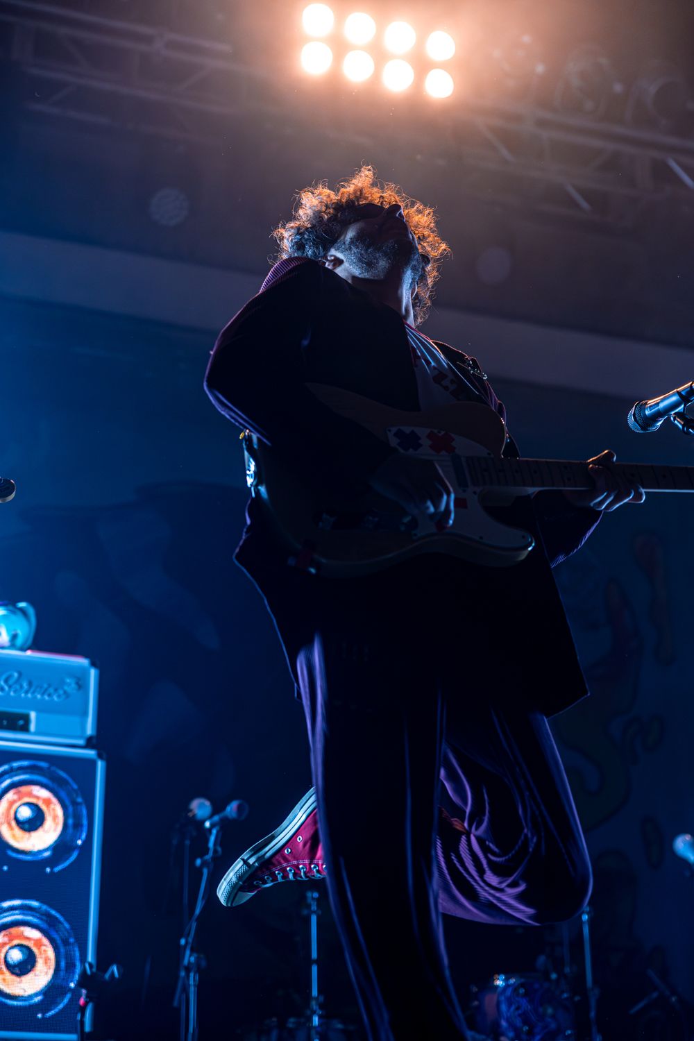 Silhouetted performers on a dimly lit stage with blue lighting and illuminated speakers in the background.