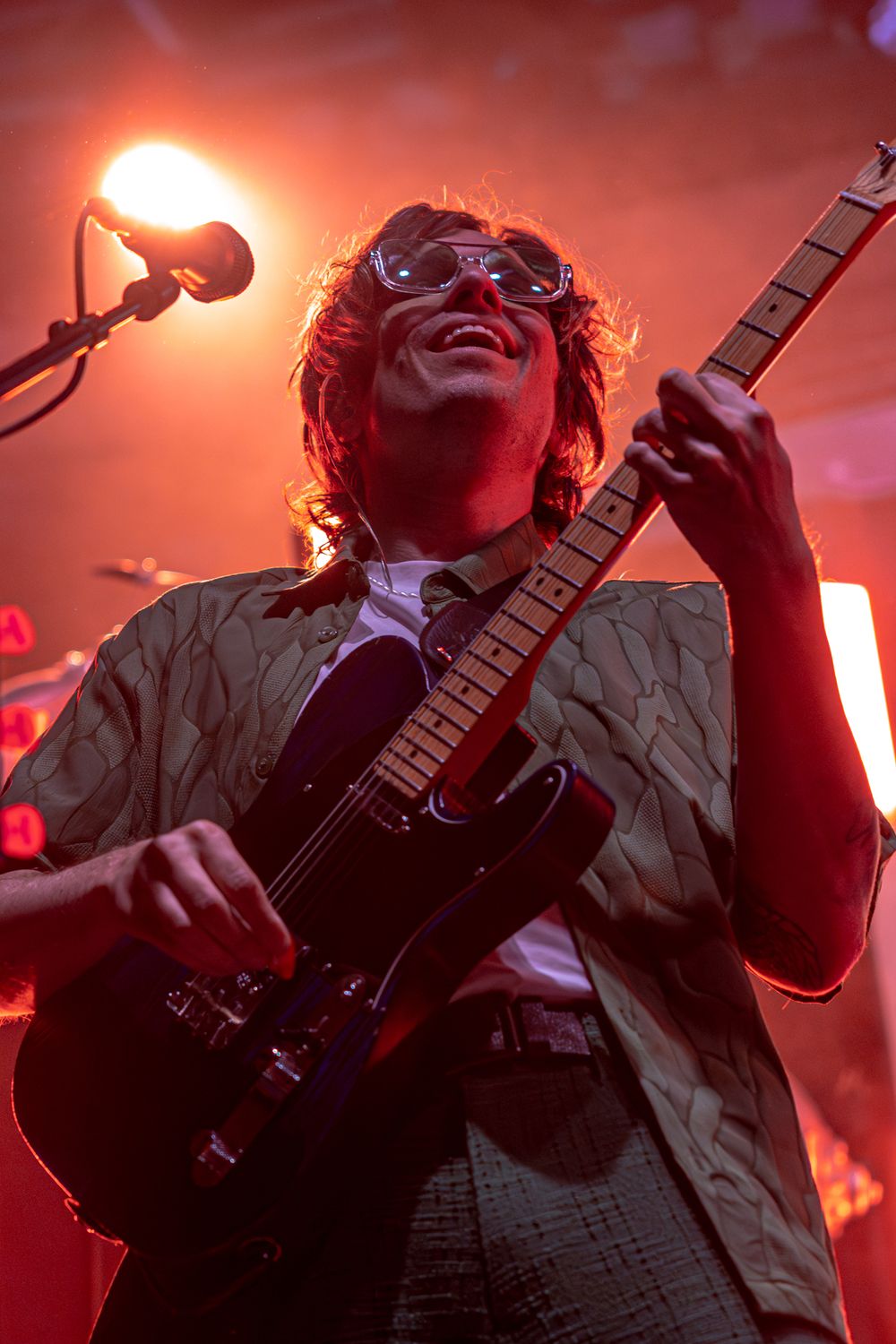 Musician in dramatic red lighting performs passionately on stage with an electric guitar during a rock concert.