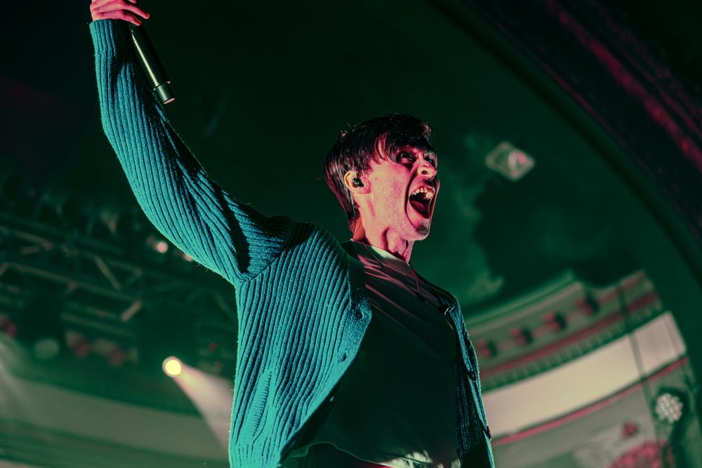 A performer in a turquoise outfit dances energetically on stage under dramatic lighting.