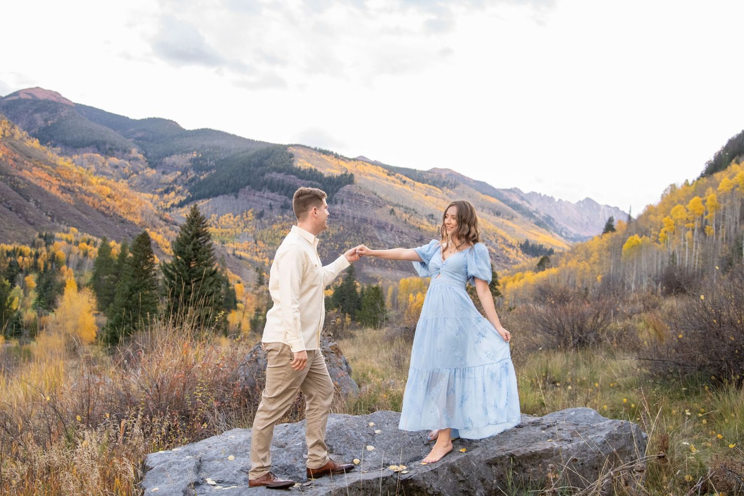 Vail engagement photos with a couple in fashionable attire poses together in a scenic mountain landscape with golden autumn foliage.