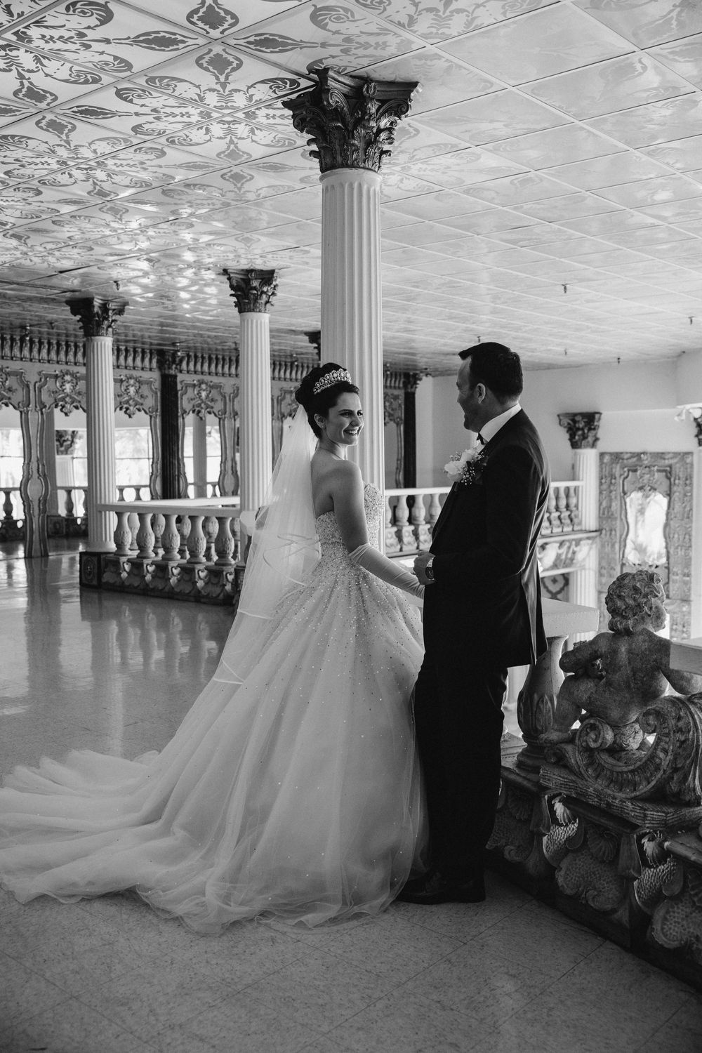 Black and white wedding photos in an ornate ballroom with classical columns and decorative ceiling.