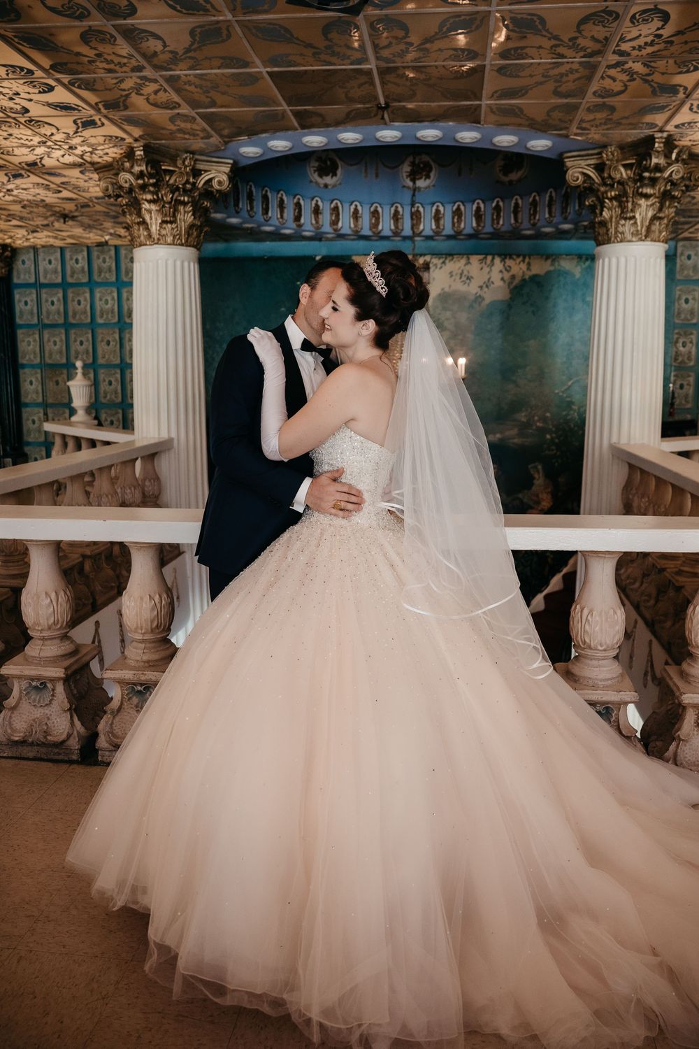 Romantic wedding moment captured in an elegant venue with ornate columns and dramatic lighting.