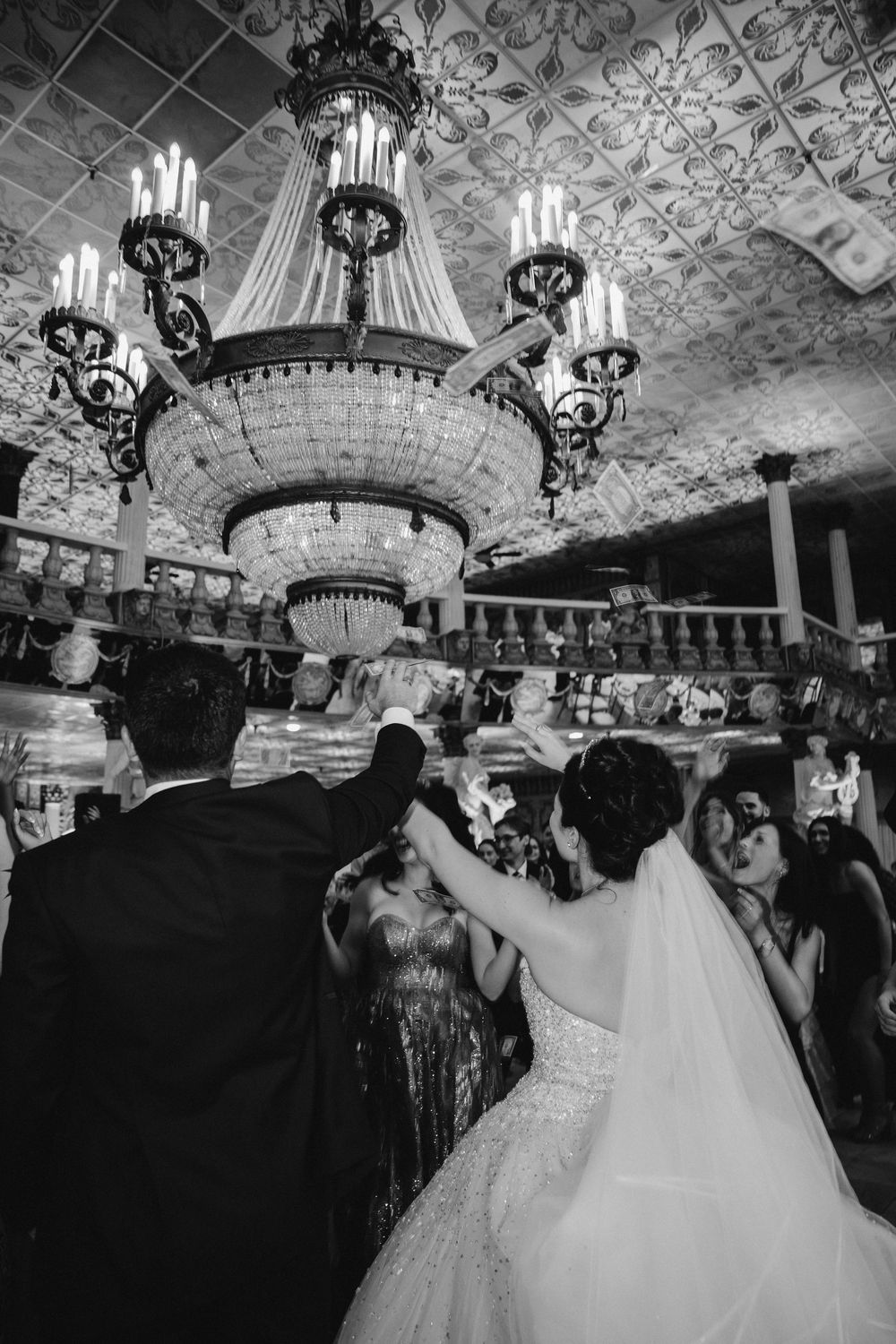 Black and white panorama of wedding reception with ornate ceiling chandeliers.
