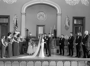 Black and white panoramic view of a wedding ceremony in an ornate classical room.