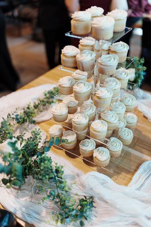 White frosted cupcakes arranged on tiered stands with eucalyptus decorations.