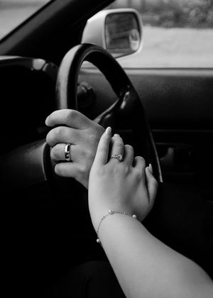 Hands resting on steering wheel showing wedding rings and bridal manicure.