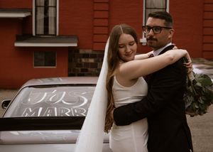 Newlyweds embrace in front of a classic red brick building during their wedding celebration.