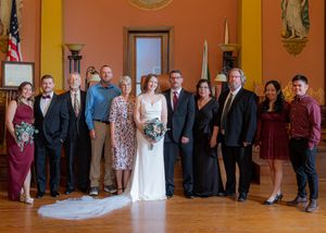 Wedding party and guests line up for a group photo in an orange-walled room.