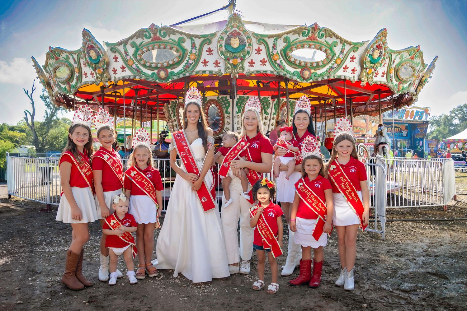 A group in red and white outfits poses together at a carnival with rides and attractions visible in the background.