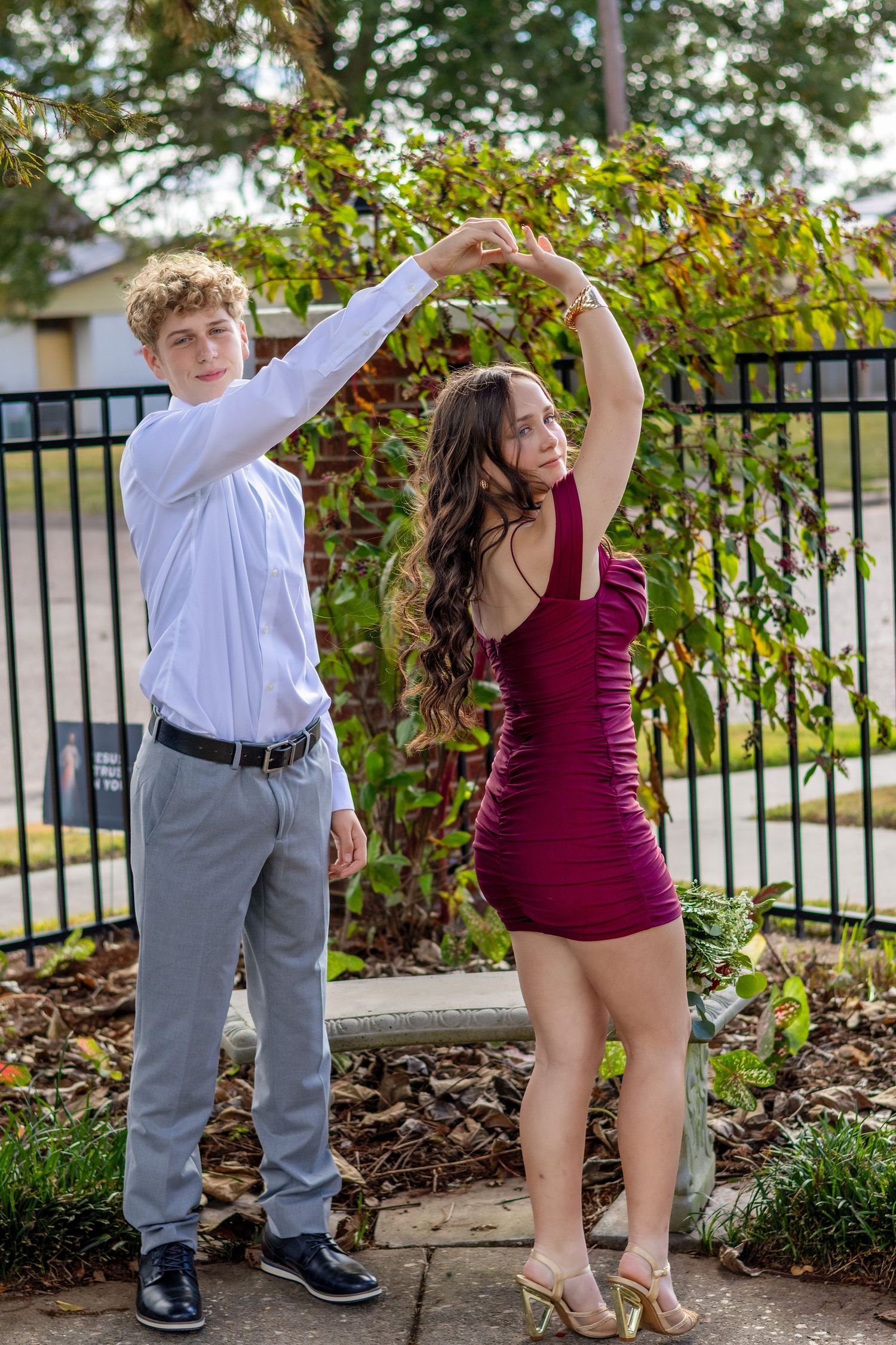 A couple dances and poses playfully outdoors in formal wear with burgundy and white color scheme.