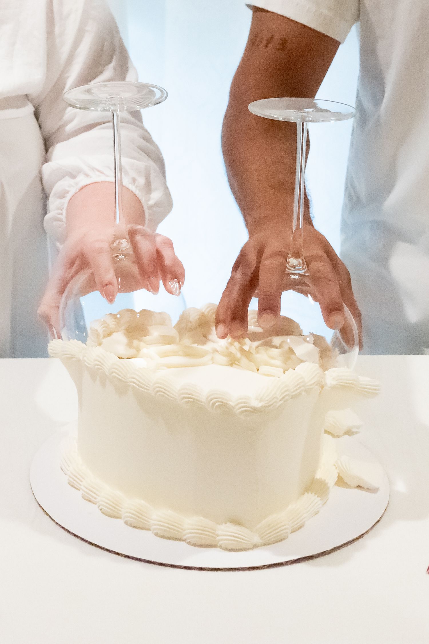 Hands decorating a white frosted cake with piping techniques using a pastry bag to create detailed patterns.