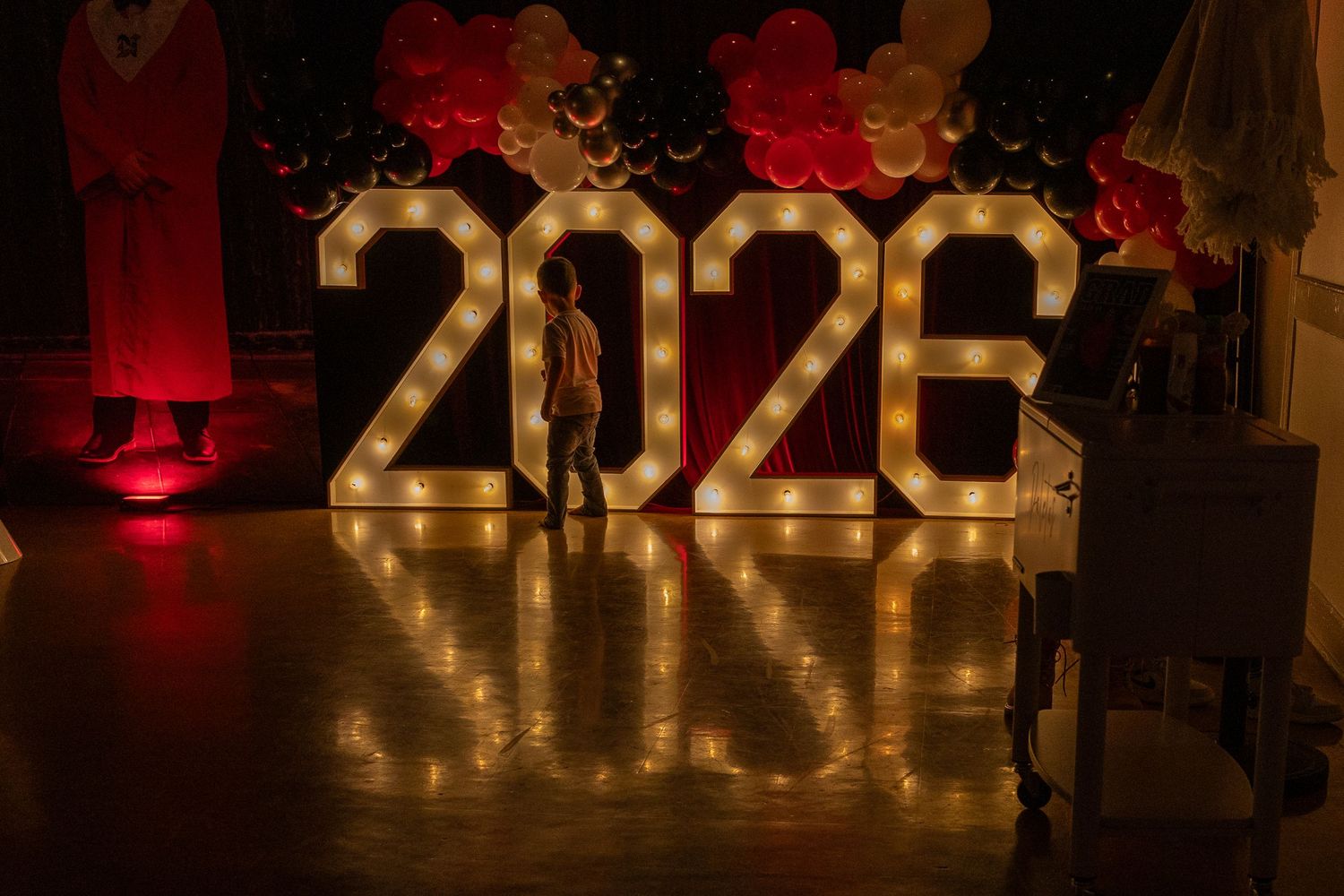 Illuminated marquee 2026 sign with light bulbs on dance floor surrounded by red and white balloons at graduation party.