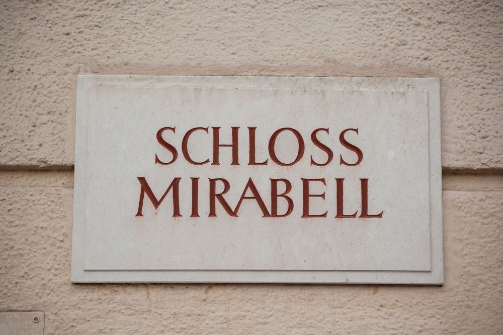 Stone wall with text signs reading 'Schloss' and 'Mirabell' mounted on beige surface.