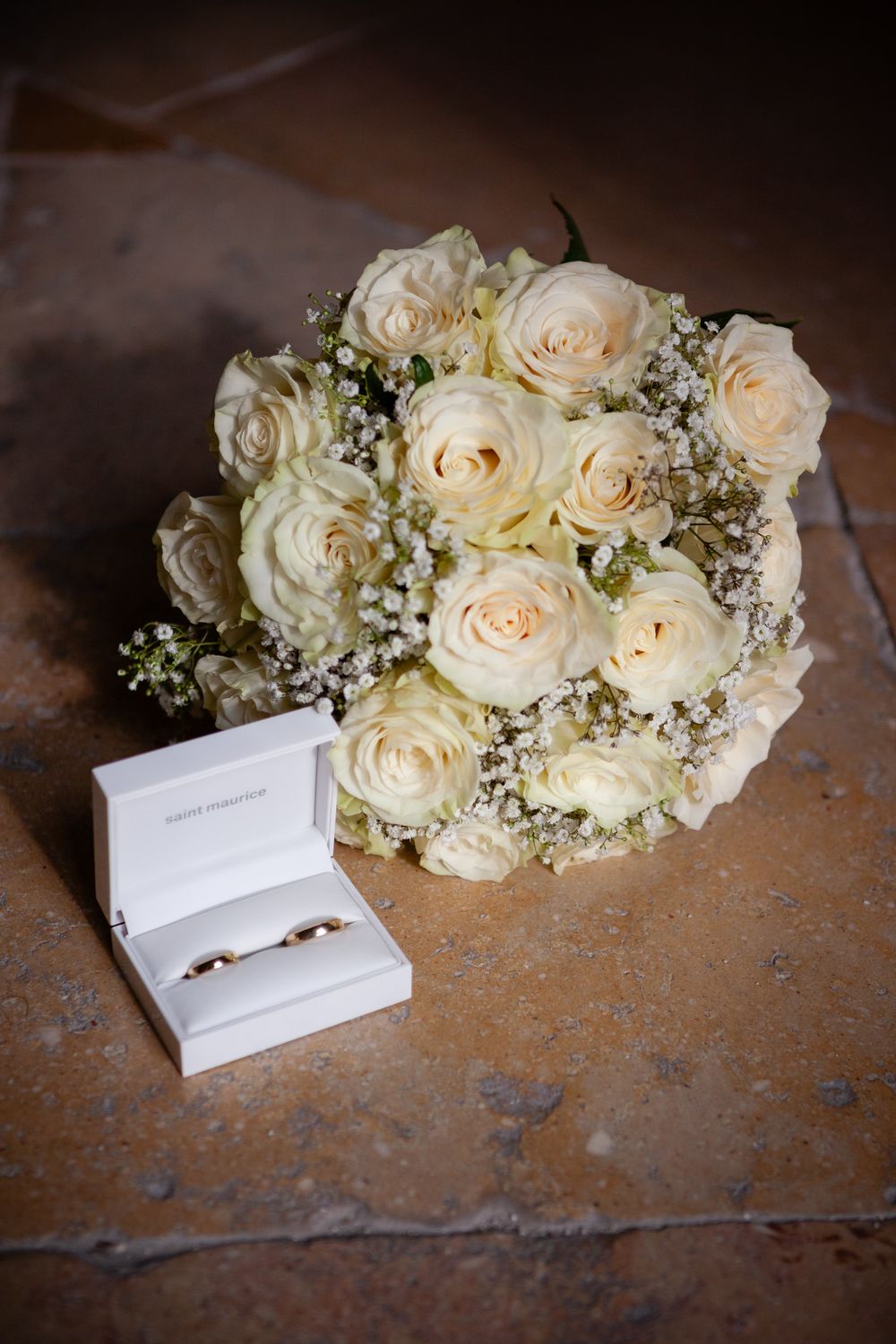 Elegant white roses and baby's breath bouquet with wedding invitation cards on a rustic wooden surface.