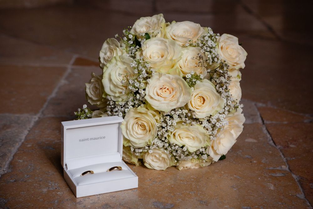 Elegant cream and white rose wedding bouquet with baby's breath on a rustic wooden surface.
