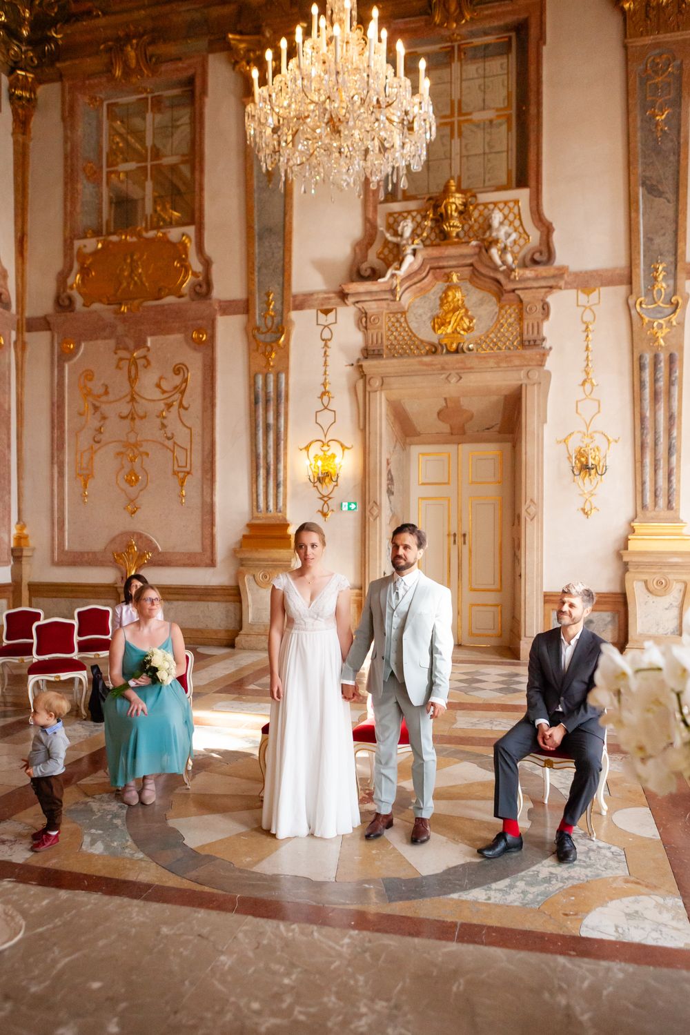 Elegant palace ballroom with ornate chandelier and baroque decor in gold and cream.