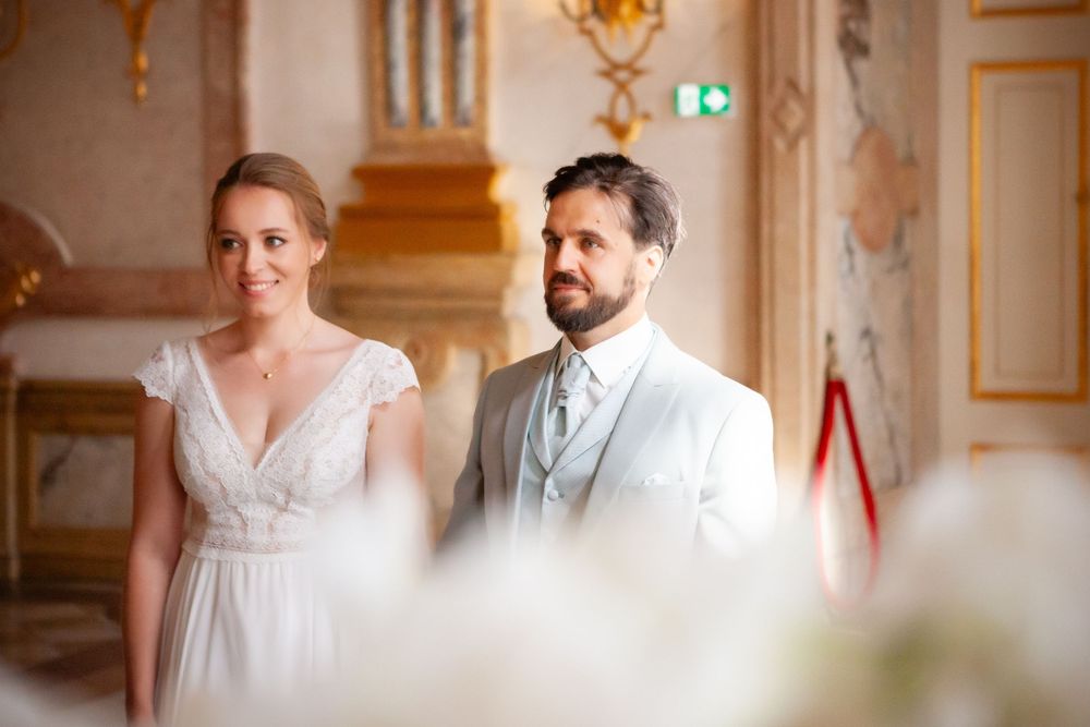 Elegant wedding couple shares intimate moments in a grand ornate room with gold decor and chandeliers.