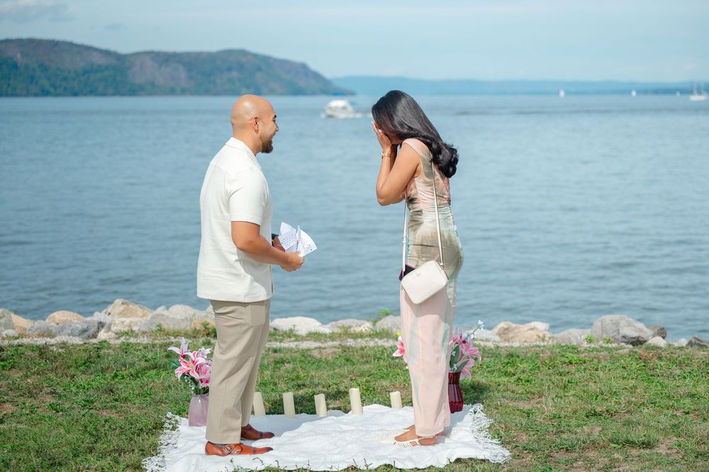 A romantic proposal scene unfolds by the waterfront with scenic mountain views in the background.