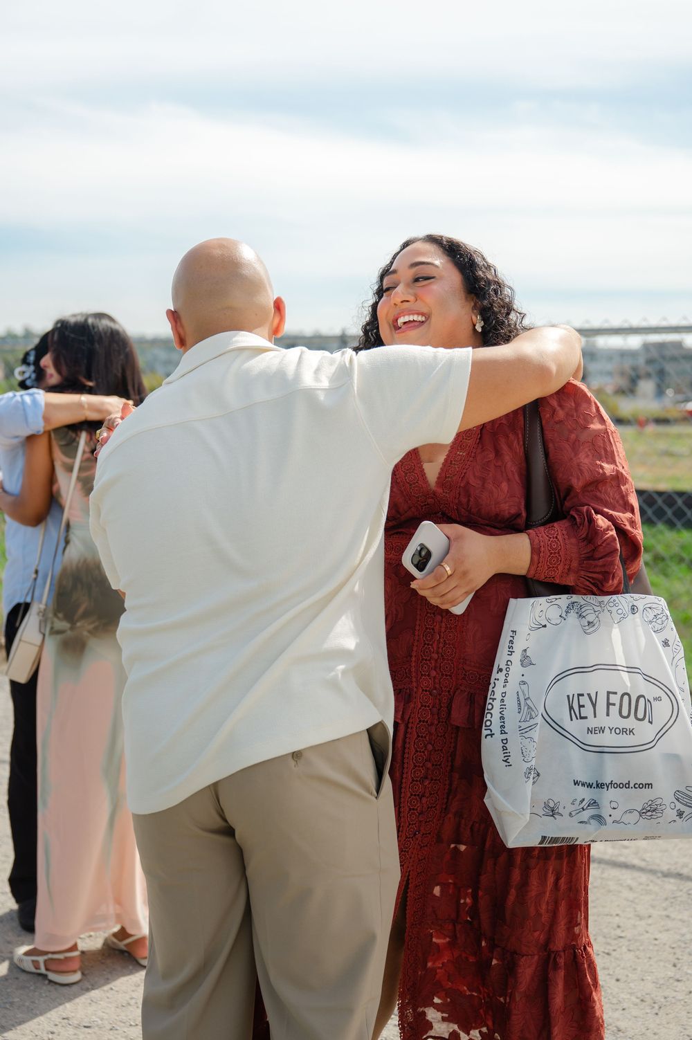 Romantic couple embracing and laughing together during a seaside photoshoot with shopping bags visible.