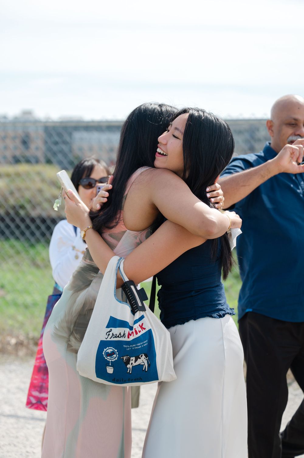 A joyful celebration moment captured at an outdoor seaside location with people embracing.