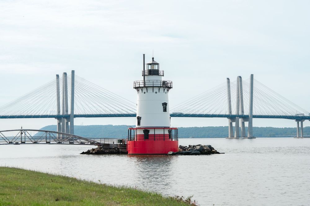 Lighthouse and suspension bridge towers of the Tappan Zee Bridge rise above the water on a misty morning at Tarrytown, New York.