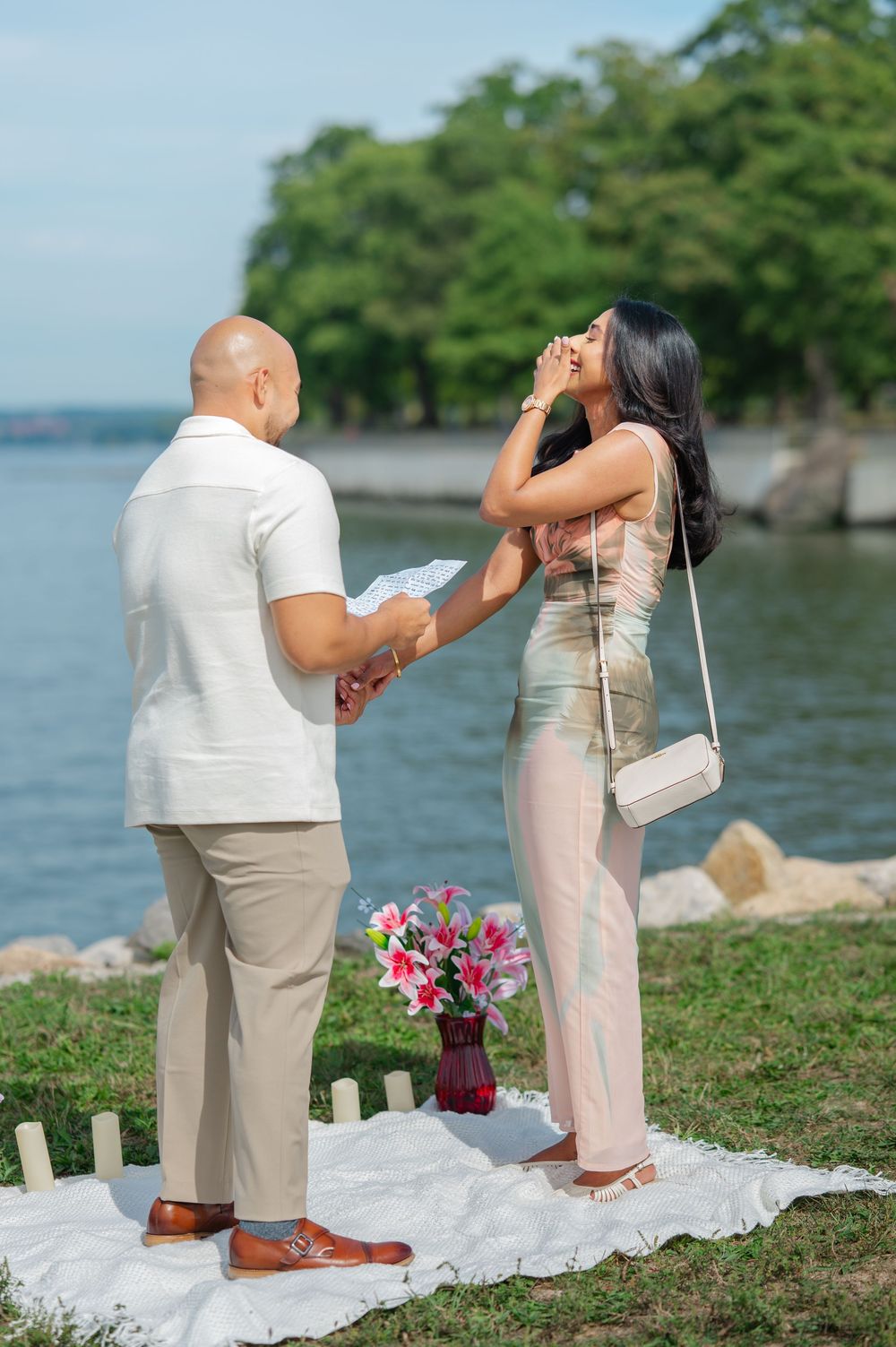 A romantic proposal sequence by the water showing a couple in white and beige outfits with pink flowers on display along the Hudson River.