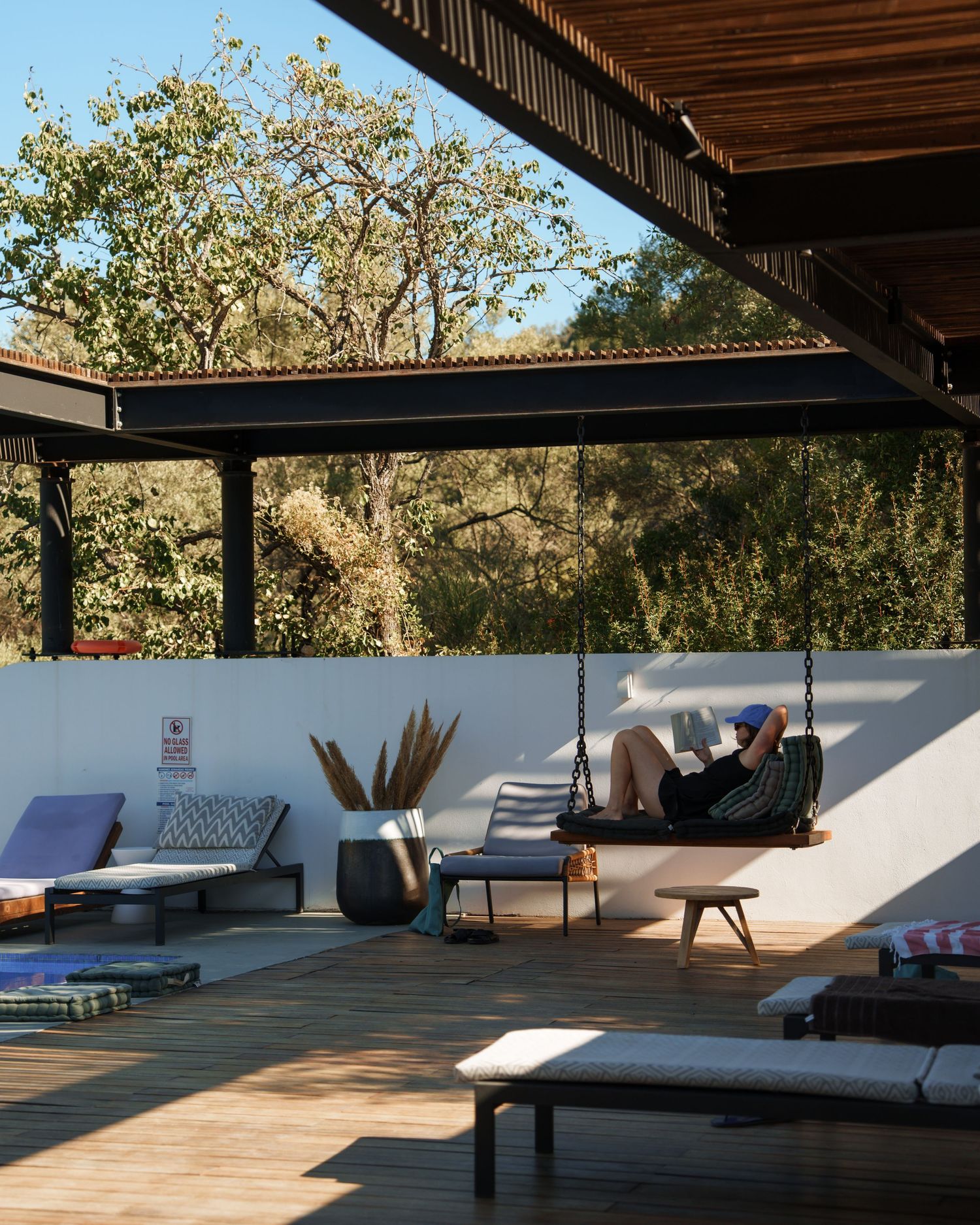 Modern outdoor yoga studio with wooden deck and white walls features lounge chairs and meditation cushions under a shaded roof.