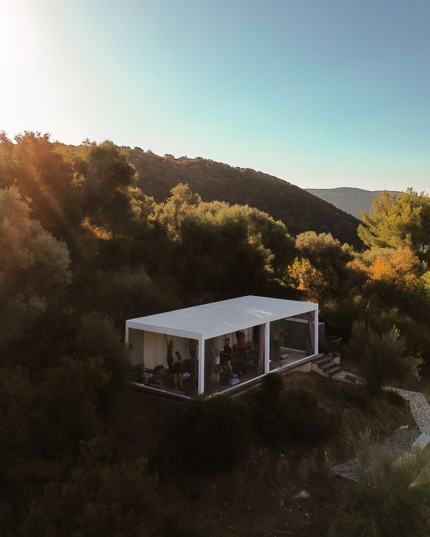 Modern white pavilion structure perched on a hillside during golden hour with mountains in the background.