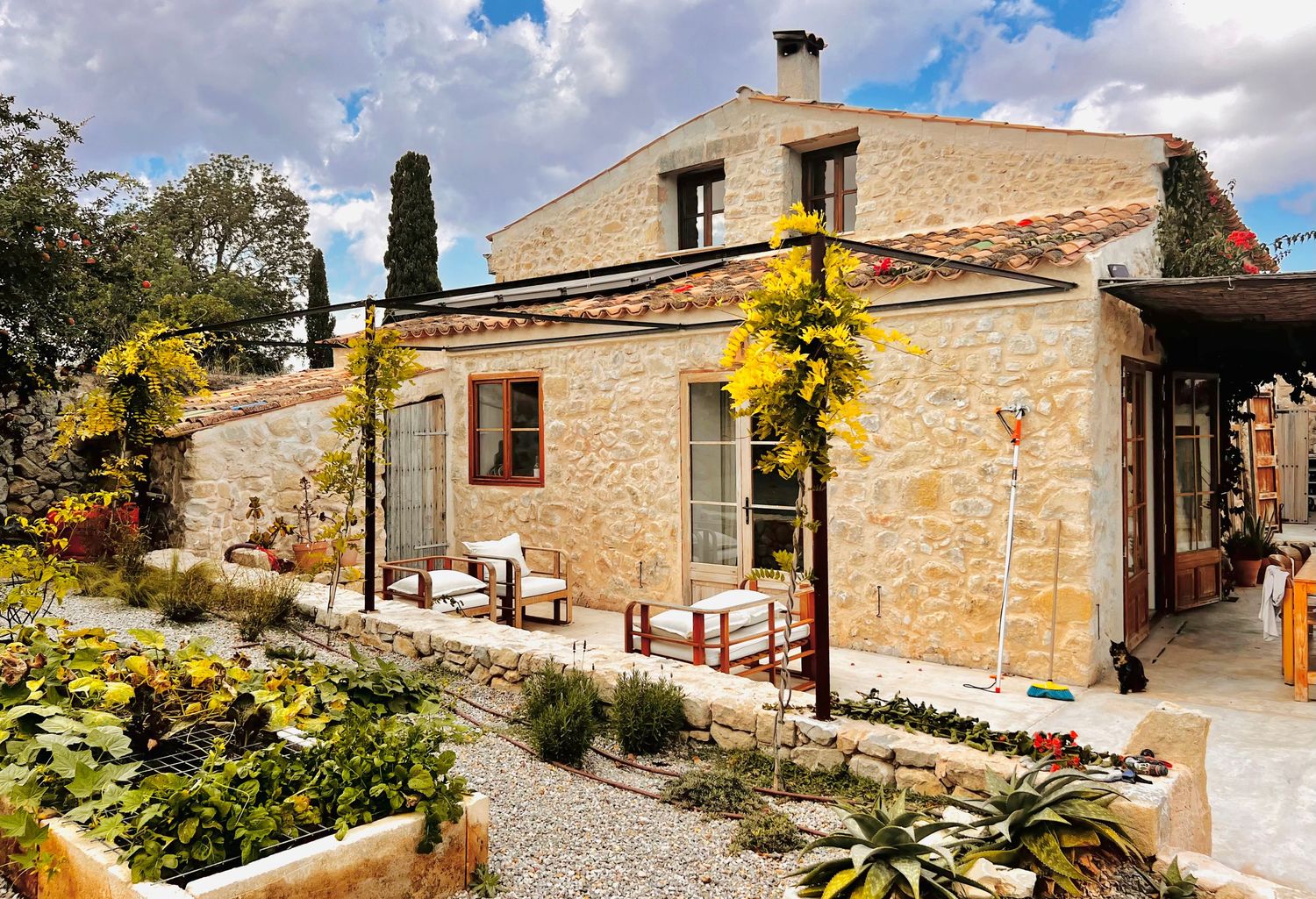 Stone villa with rustic architecture and landscaped gardens set against a blue sky in Mediterranean setting.