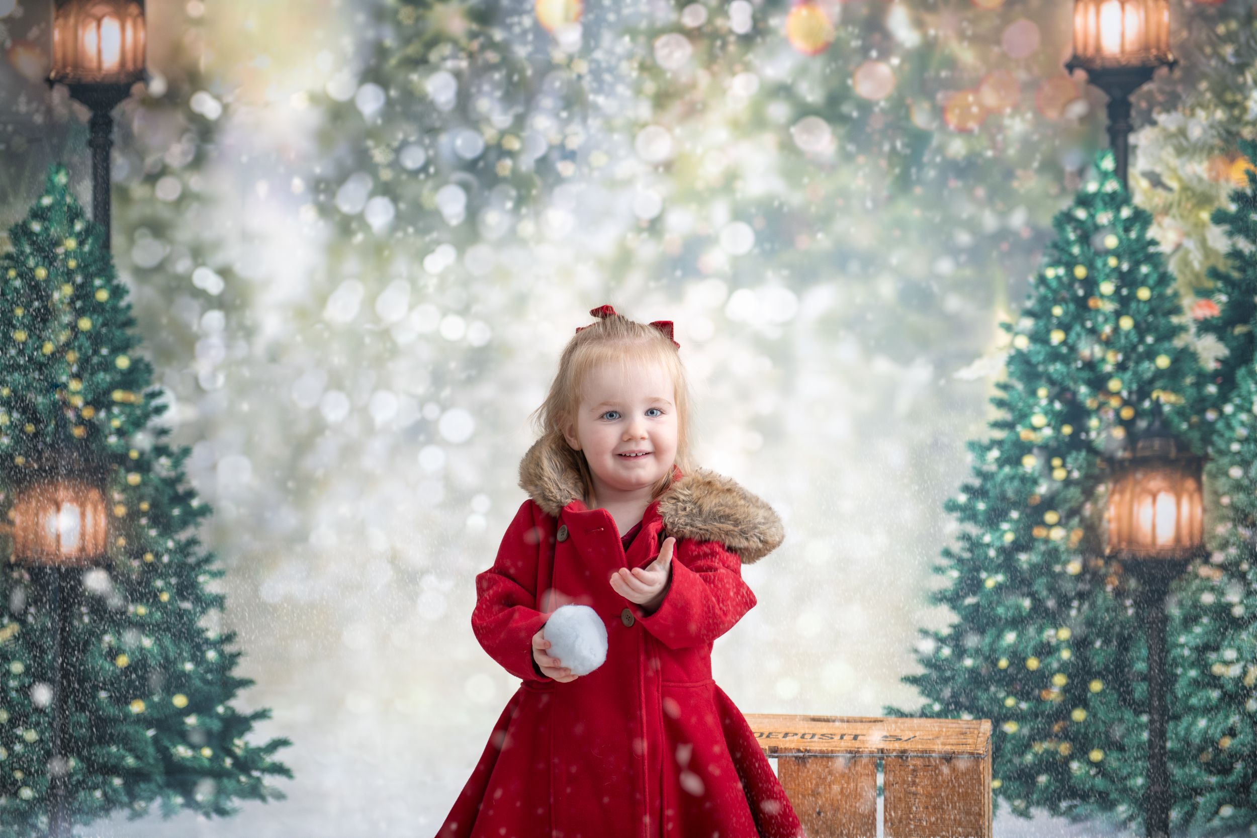 Festive holiday scene with decorated Christmas trees, glowing lanterns, and a small child in a red dress holding a snowball.