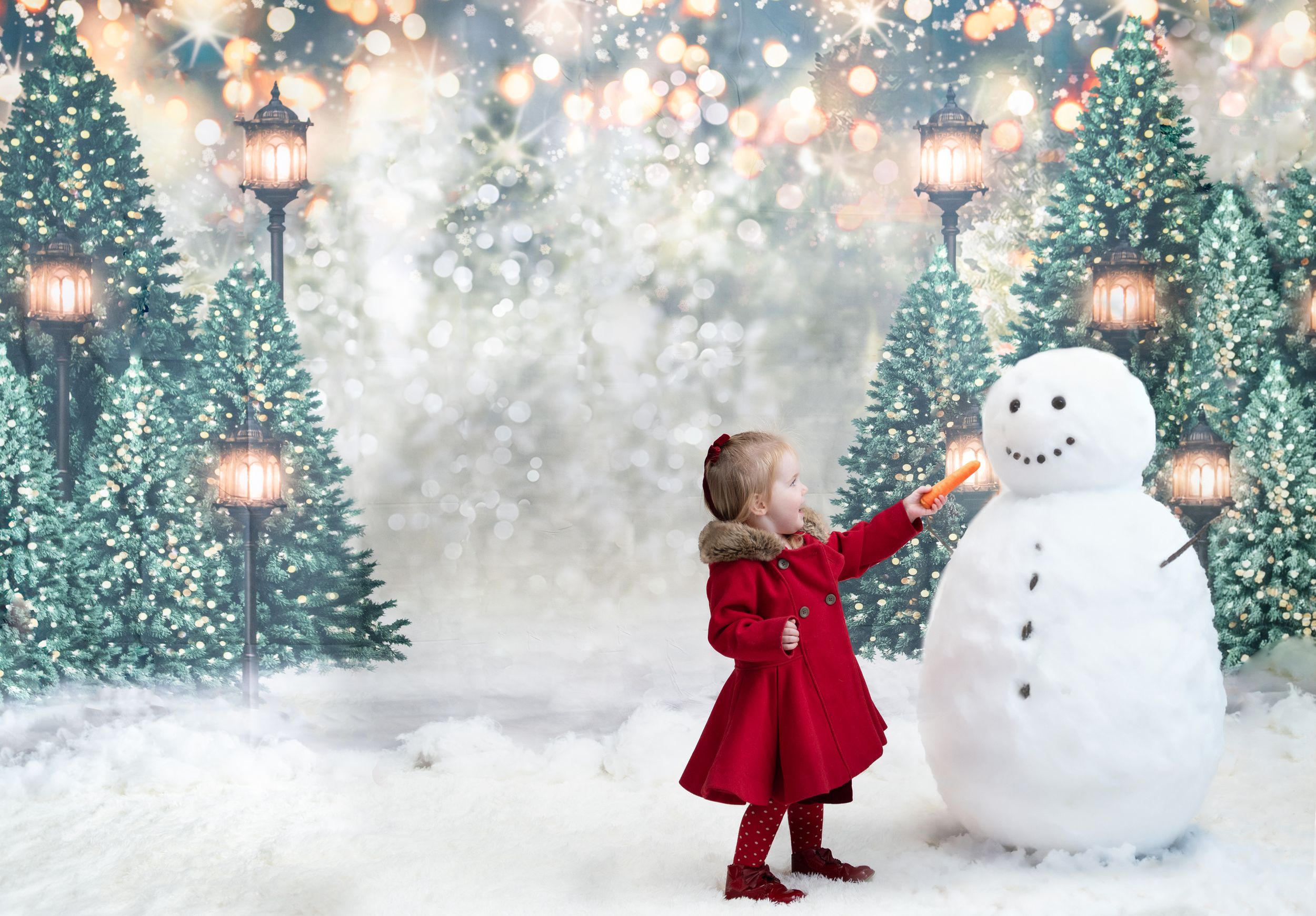 A magical winter scene shows someone in a red coat building a snowman in a snowy forest with twinkling lights.