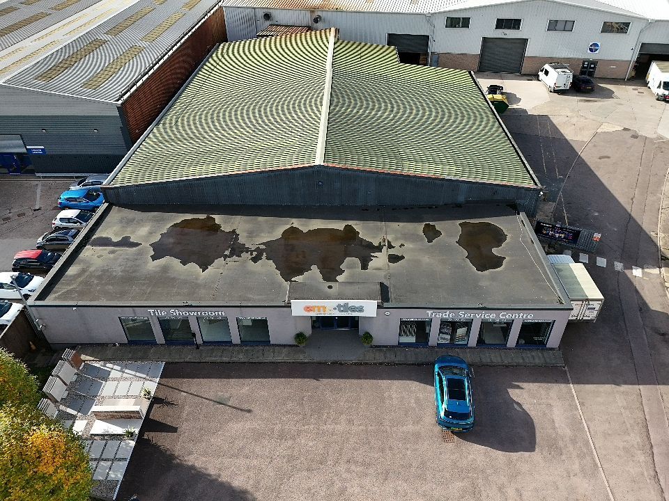 Aerial view of a commercial building with a curved green roof design and white exterior walls.