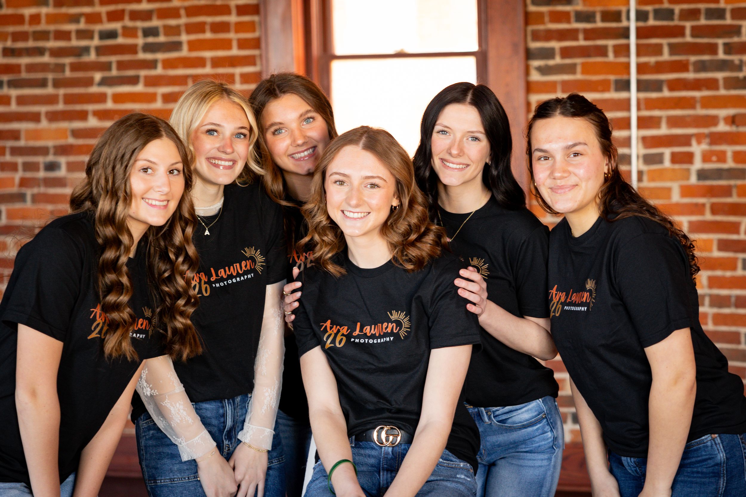 Group of people in black shirts and jeans posing together against a brick wall.