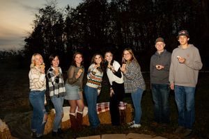 Group of friends standing together at dusk against a dark treeline silhouette.