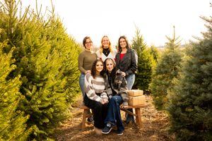 A group of people pose together outdoors among evergreen trees during a sunny autumn day.