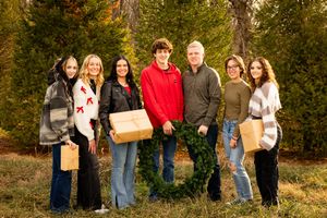 People walking together through an autumn forest path carrying gift boxes and wearing casual attire.