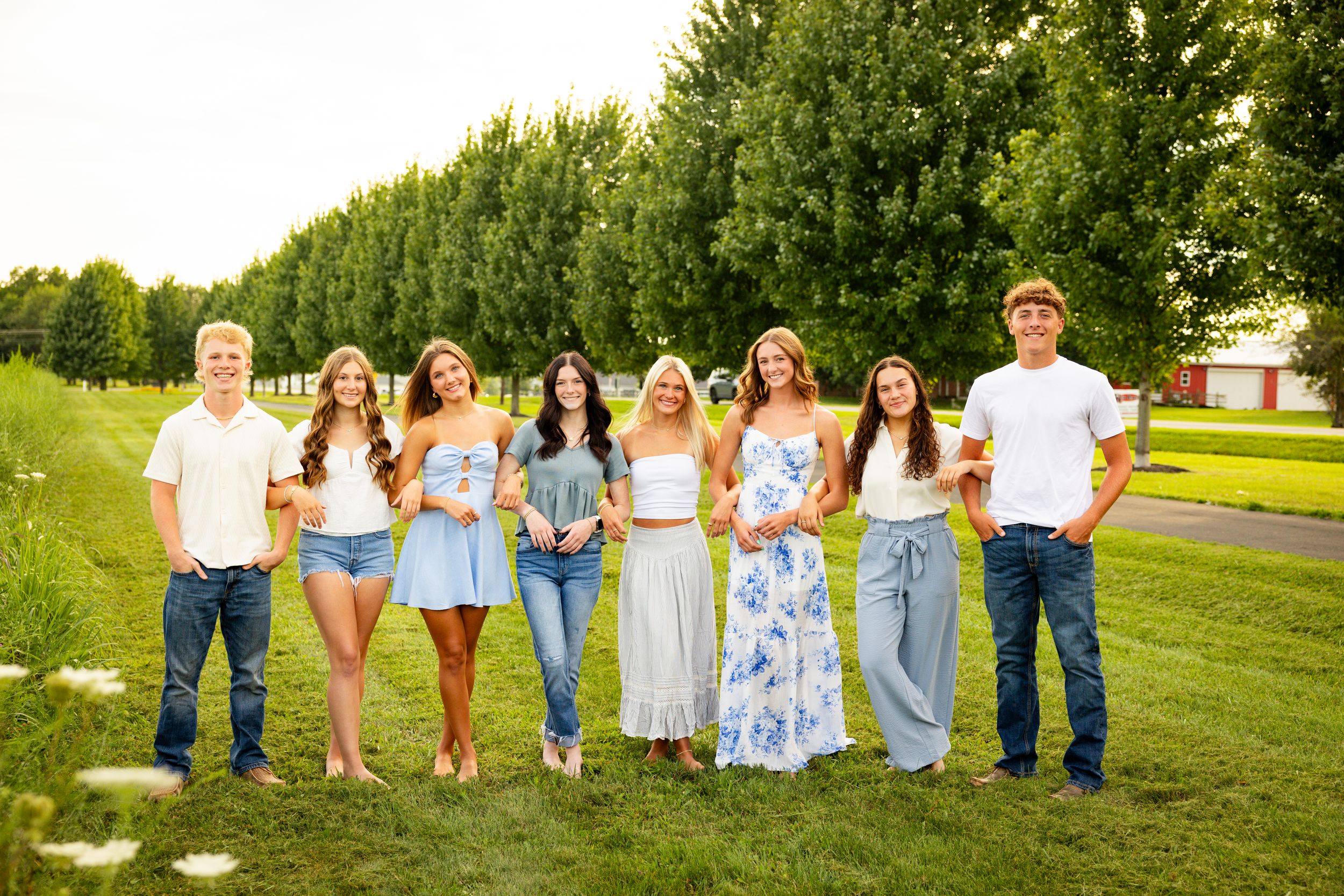 A group of people in coordinated blue and white outfits pose together on a grassy lawn during a summer photoshoot.