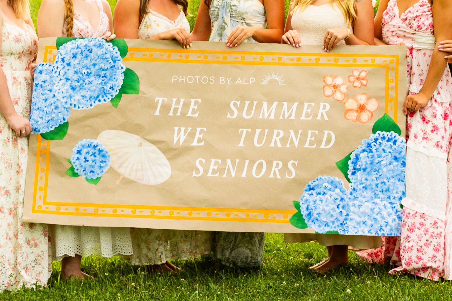 Group of girls holding a decorative sign reading The Summer We Turned Seniors with blue hydrangea flowers.