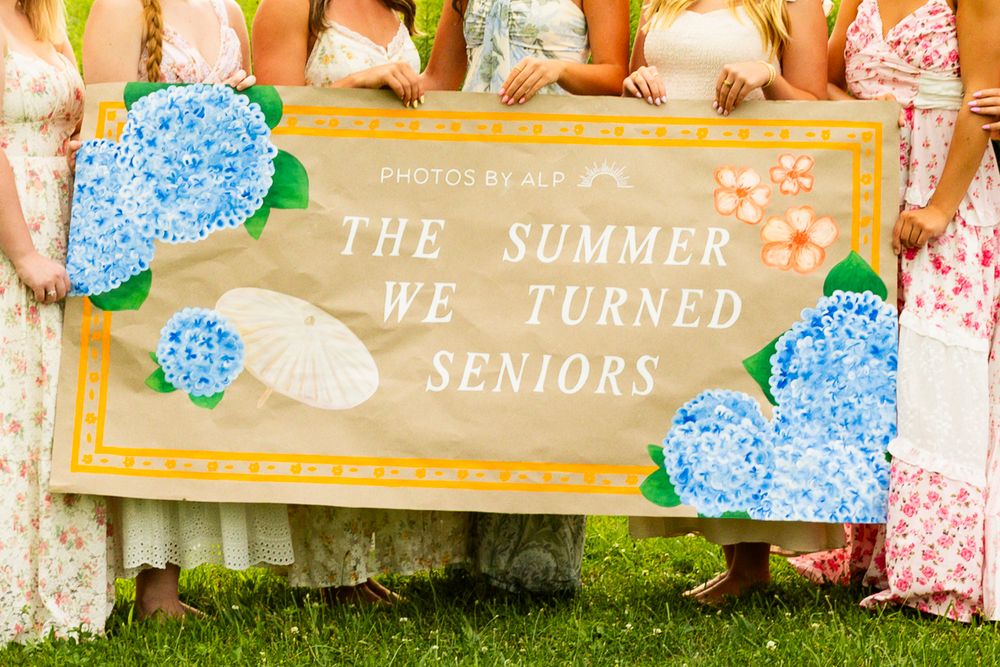 Group of girls holding a decorative sign reading The Summer We Turned Seniors with blue hydrangea flowers.