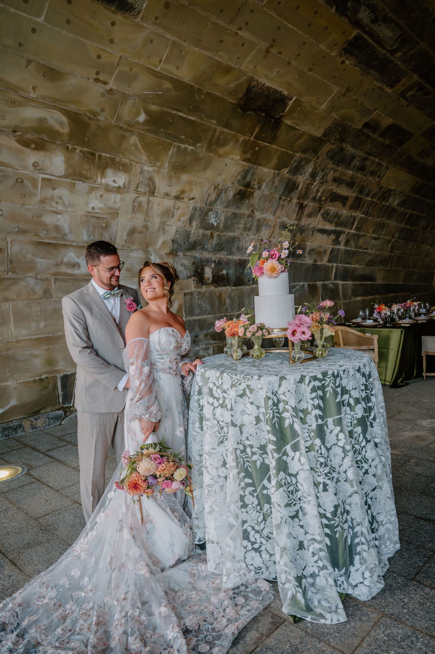Cincinnati couple at Anderson Pavilion around cake by @aspoonfullasugar and flowers by @traceyrae_farmerflorist under a stone archway.