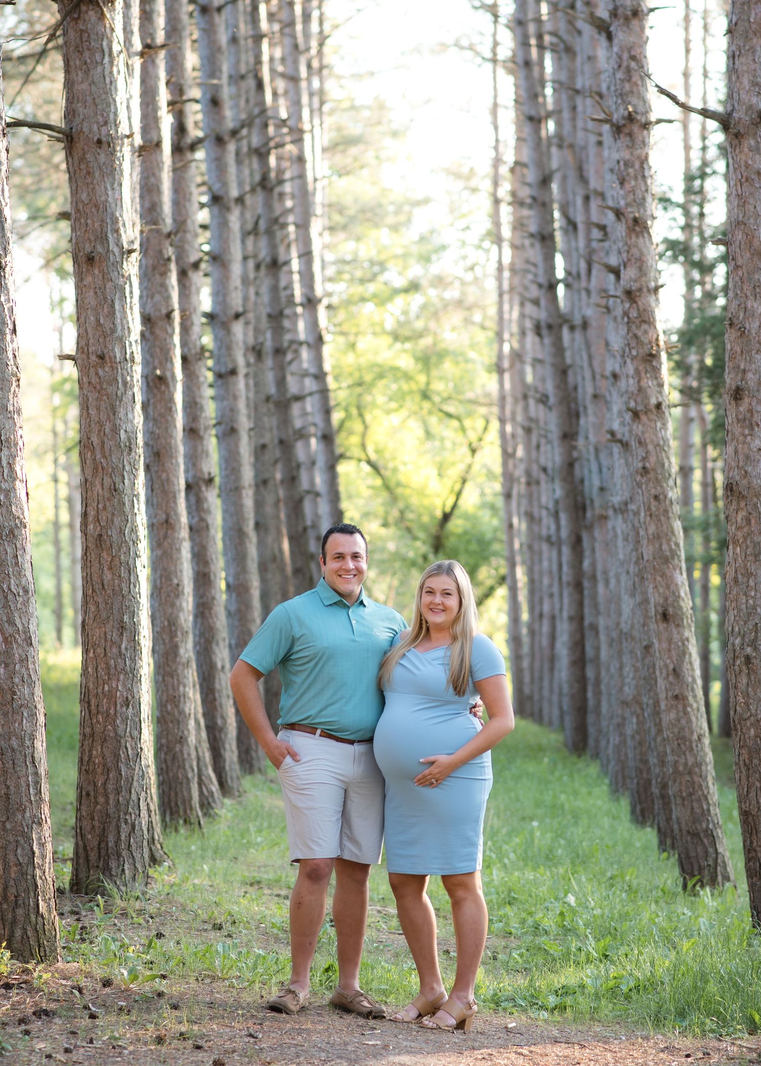 Expecting couple poses together in a scenic pine forest path during a maternity photo session.