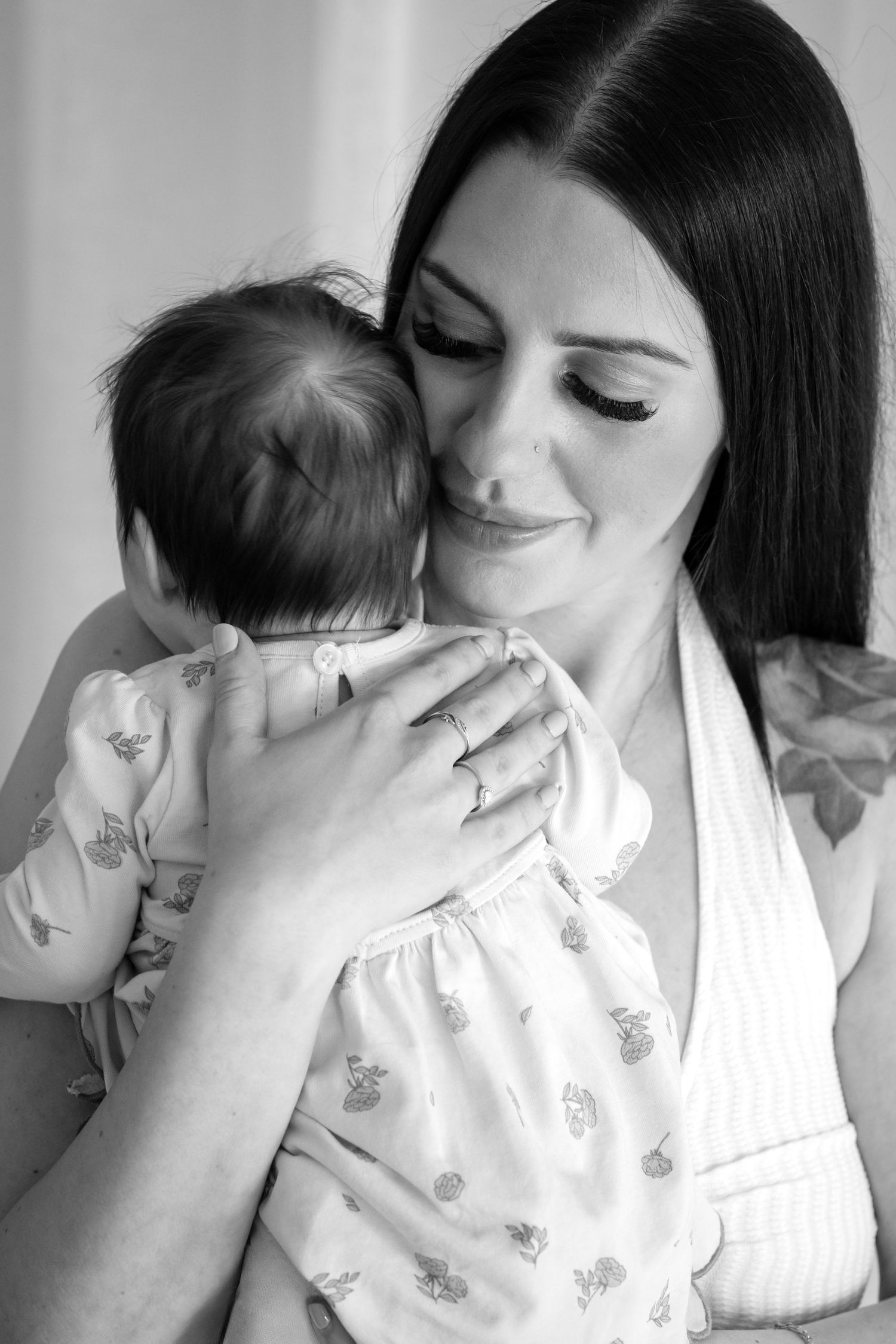 Black and white close-up photo of a newborn baby with wide eyes being kissed on the head by a parent.