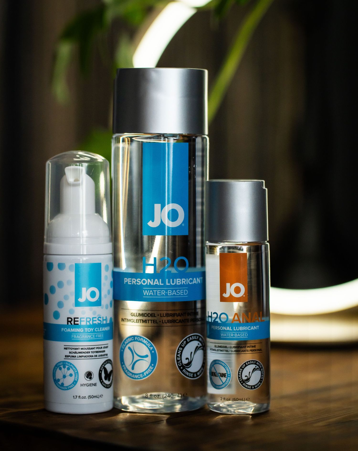 Three blue and silver personal lubricant bottles displayed against dark background with ring light.