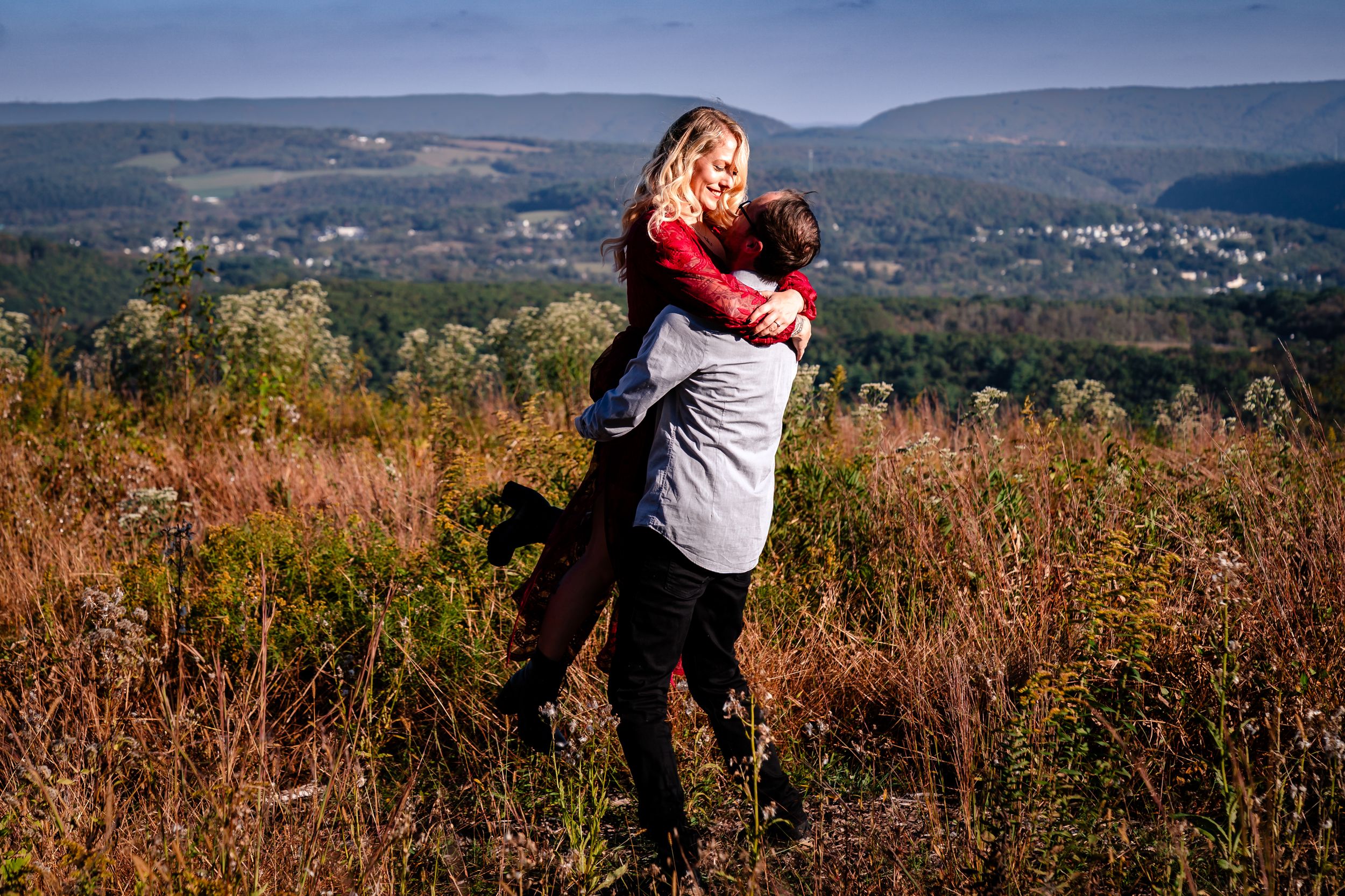 Couple embracing on mountain path with panoramic autumn landscape views.
