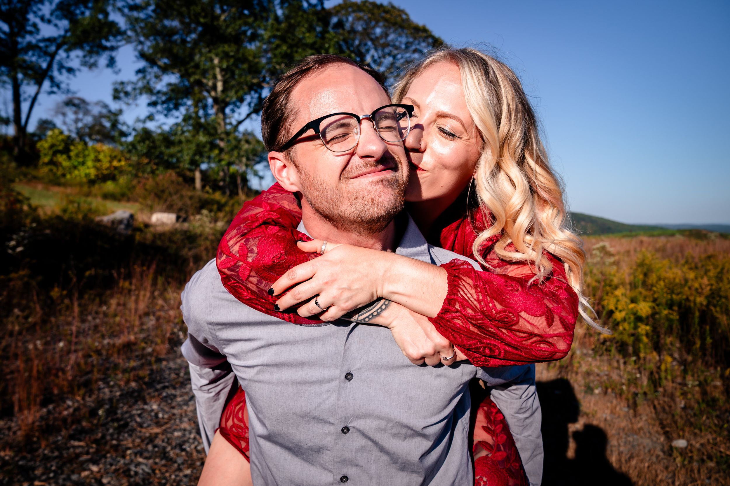 Couple sharing intimate moment outdoors with mountain scenery in background.