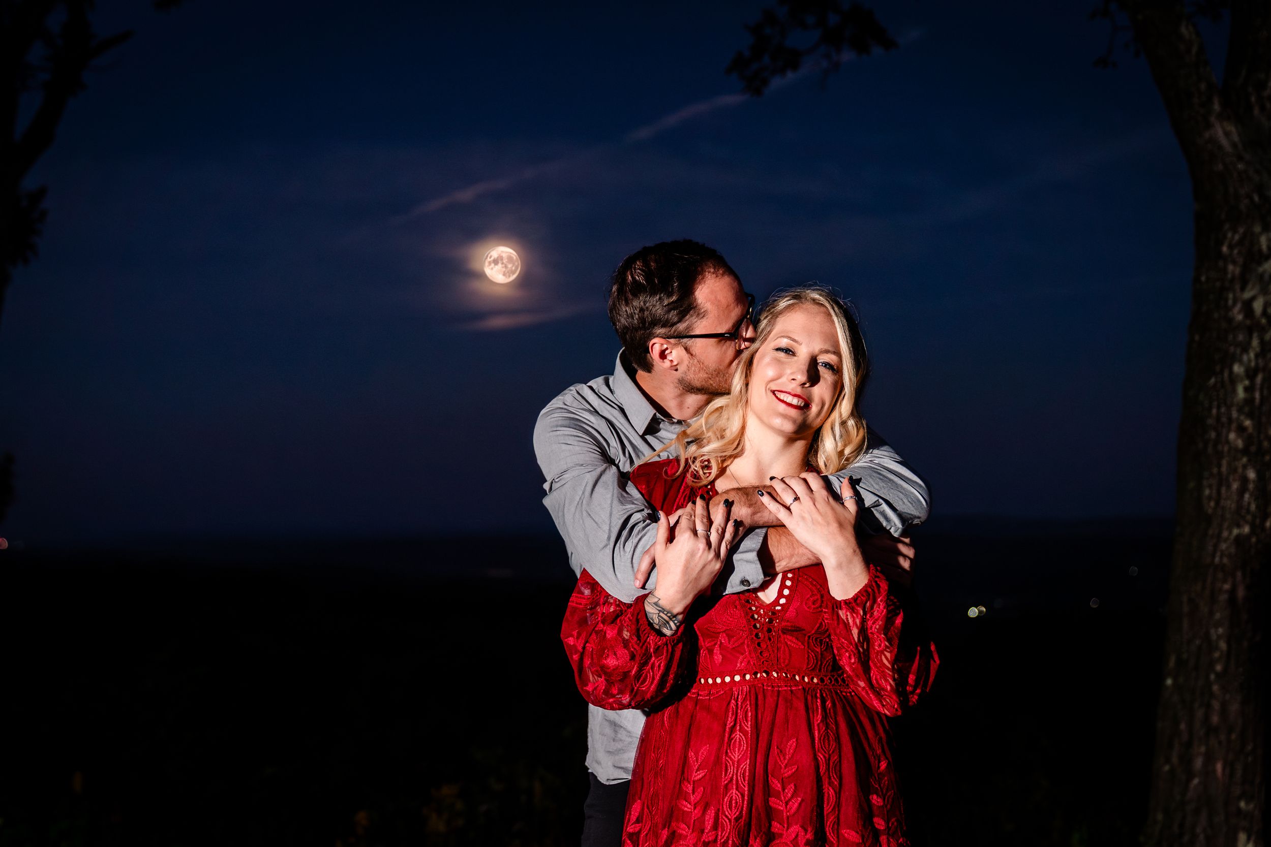 Couple sharing tender moment at night with moonlit sky backdrop.