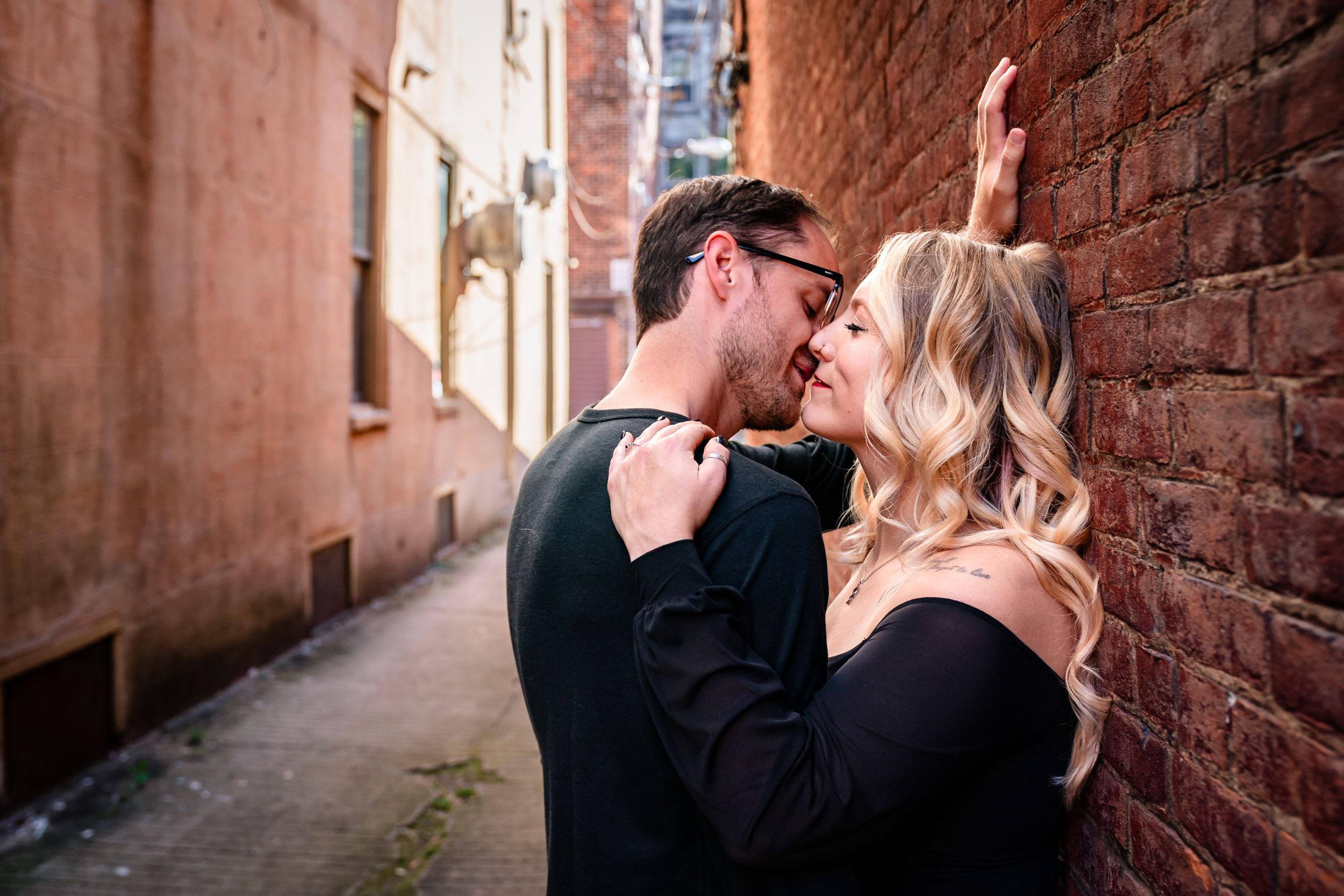 Couple embracing against rustic brick wall in an alley.