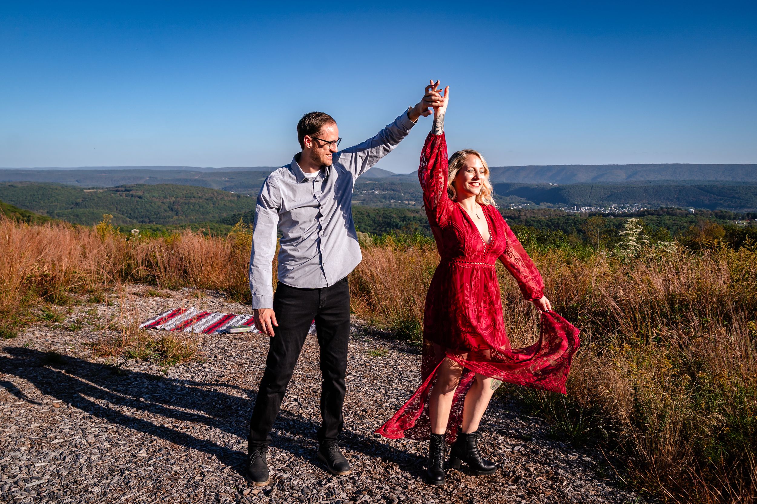 Dancing couple in scenic mountain landscape with blue skies and rolling hills in background.